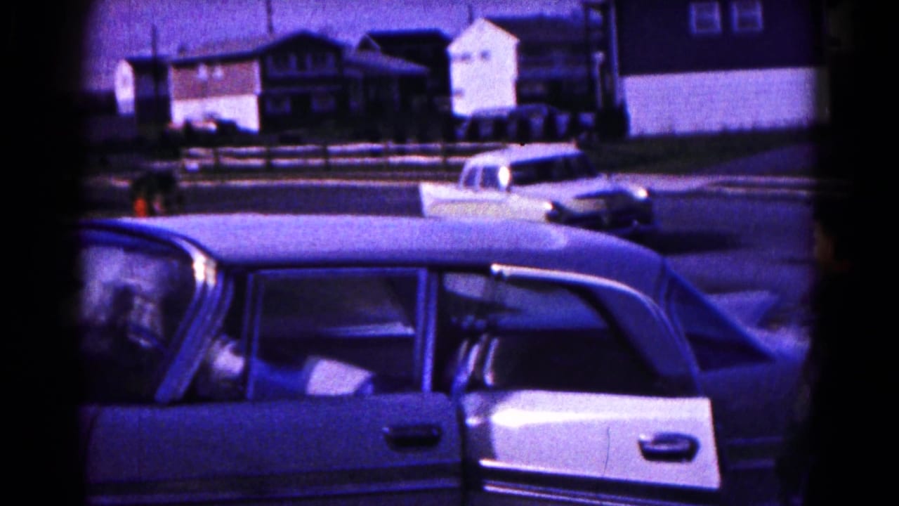 1961 Hagerstown street view with a light-colored sedan in the foreground, an open rear door, parked cars, and residential buildings beyond.