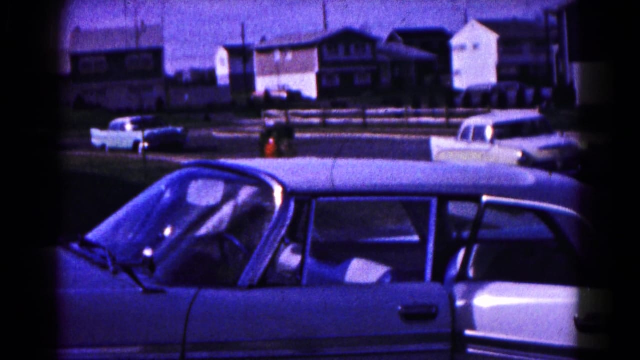 1961 Hagerstown residential street with a light-colored sedan in the foreground and period cars and houses across the road.