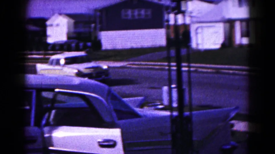 1961 Hagerstown street scene showing part of a foreground sedan, a road, parked cars, and modest homes in soft 8mm color.