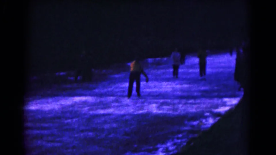 1961 Hagerstown home-movie frame showing silhouetted skaters on a blue-purple outdoor ice surface at night.
