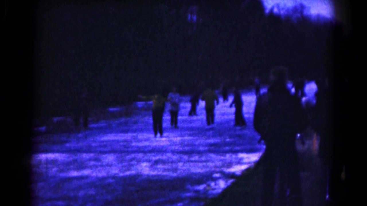 A group of skaters gathers on the illuminated ice under dark surroundings.