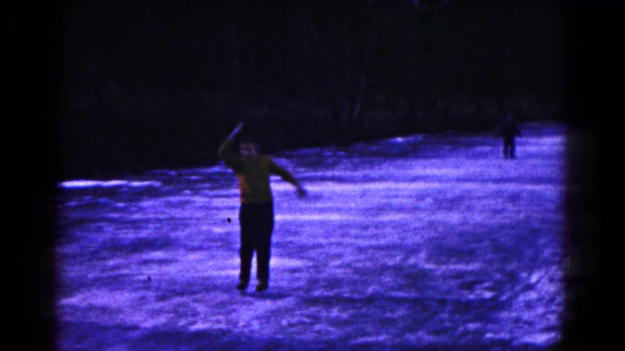A skater in a yellow top moves across a frozen pond with another person in the distance.