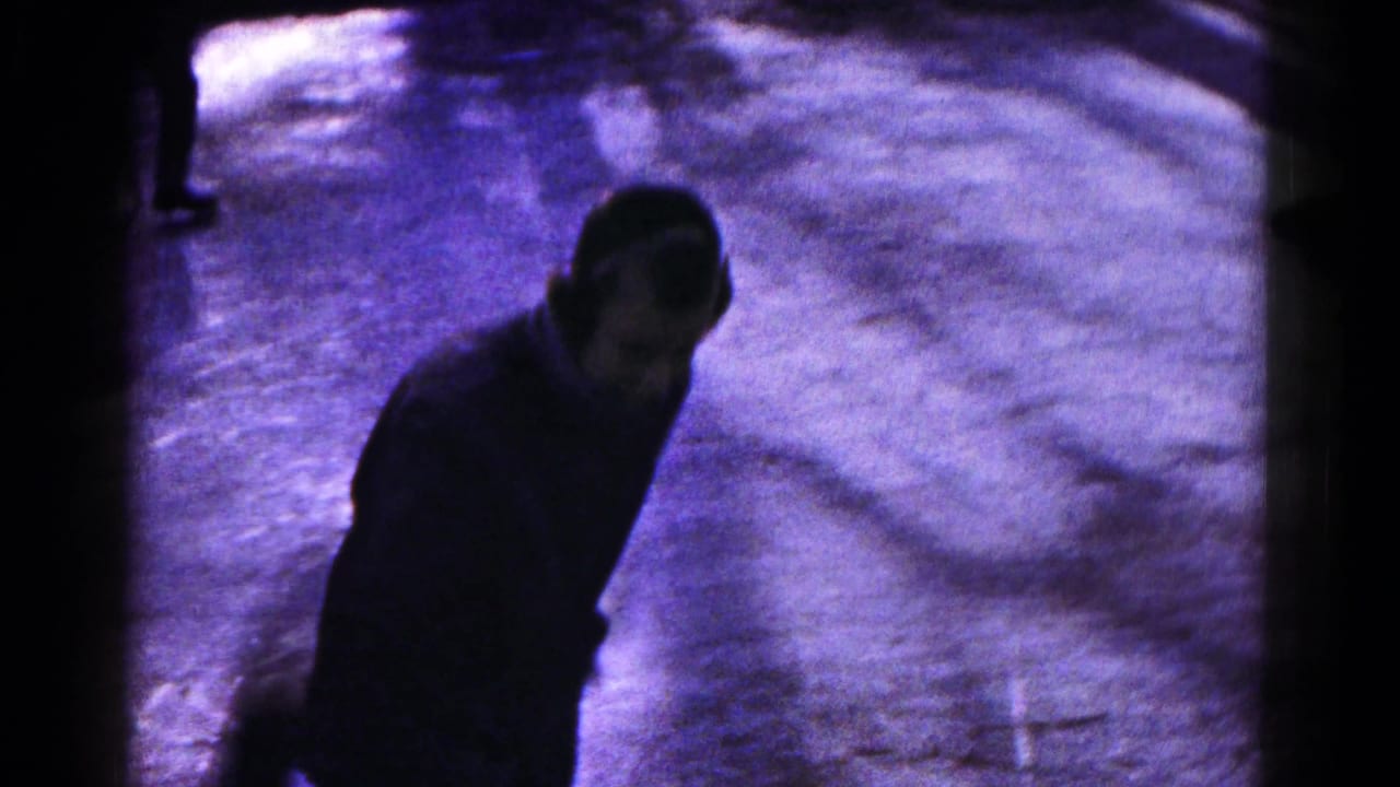 A dark-clothed skater moves across the frozen lake, partly shadowed in the 8mm winter footage from Hagerstown.