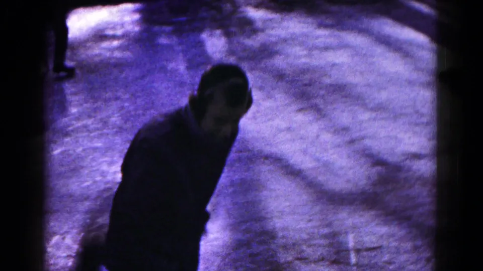 A dark-clothed skater moves across the frozen lake, partly shadowed in the 8mm winter footage from Hagerstown.