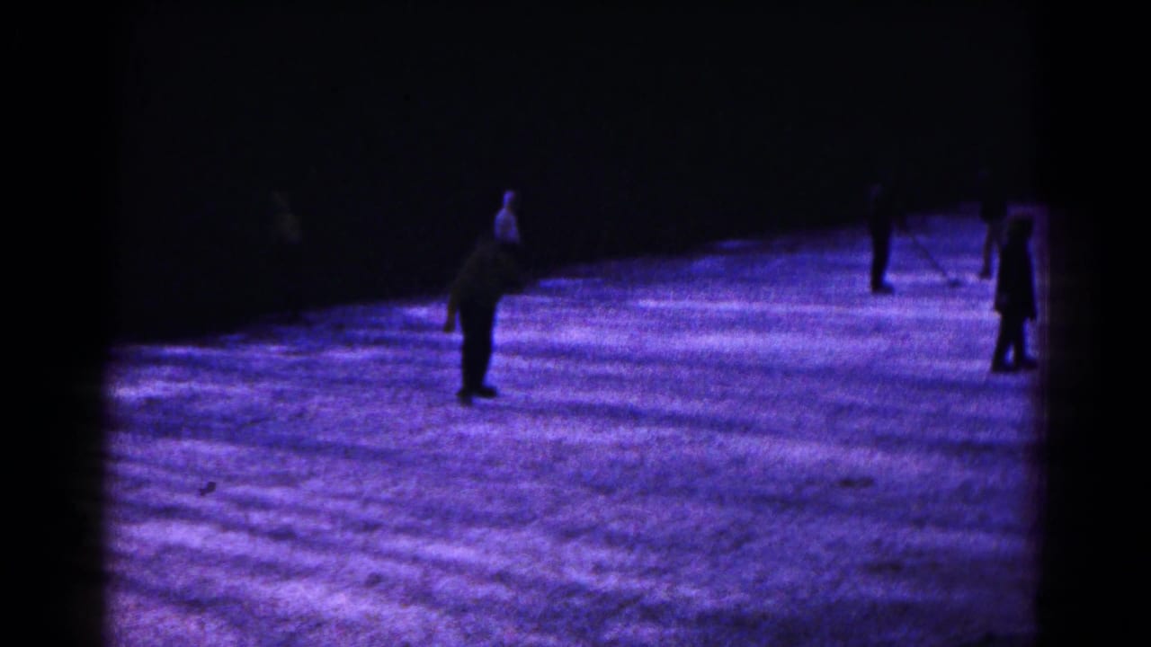 1961 Hagerstown home-movie frame showing distant skaters on a dark, purple-blue illuminated ice surface.