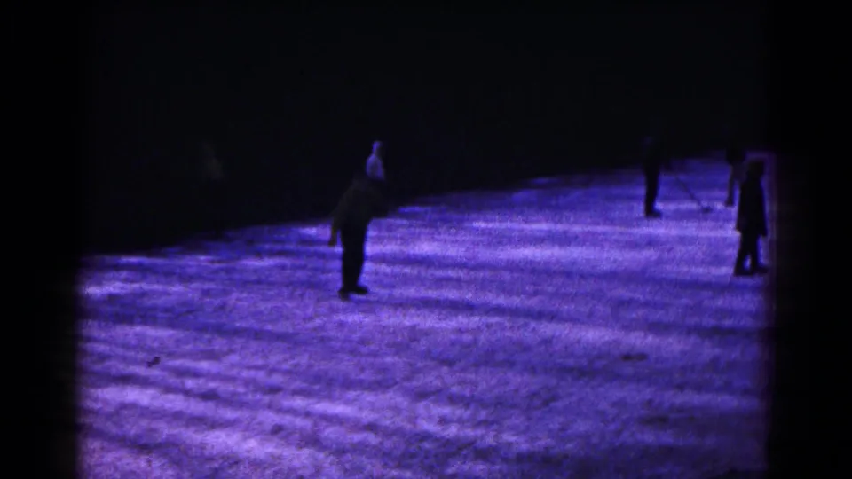 1961 Hagerstown home-movie frame showing distant skaters on a dark, purple-blue illuminated ice surface.