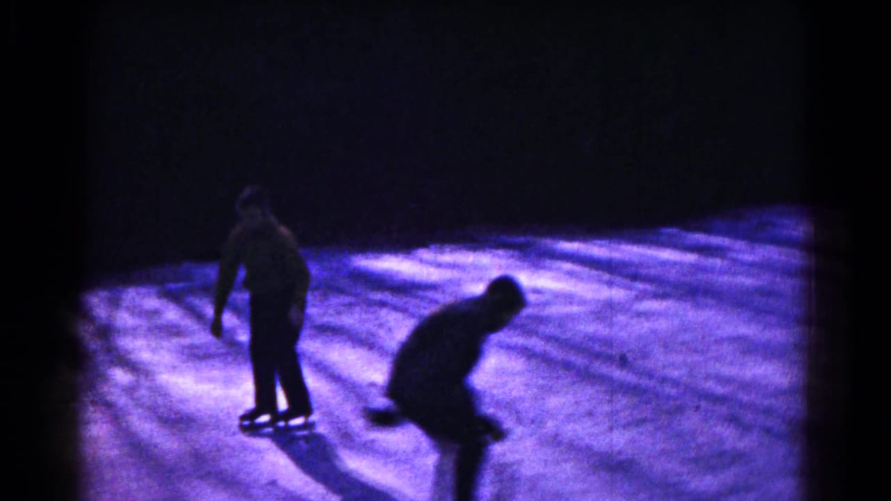 Two people skate on a dimly lit frozen surface in 1961 Hagerstown, Maryland home-movie footage.