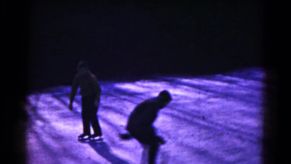Two people skate on a dimly lit frozen surface in 1961 Hagerstown, Maryland home-movie footage.