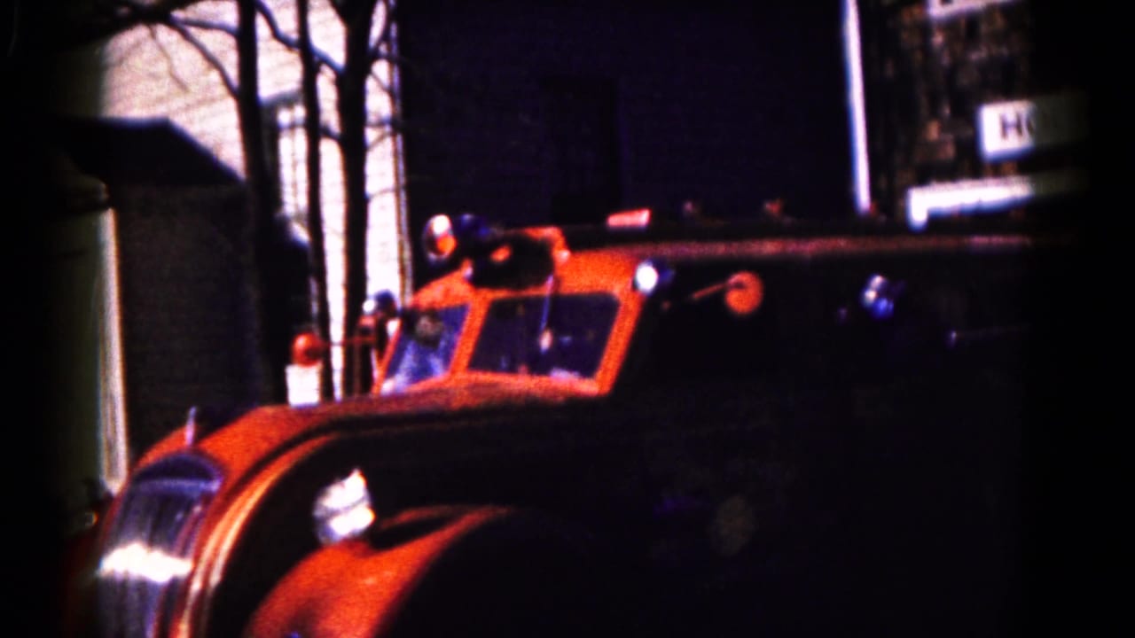 Orange-and-black vintage fire engine entering the frame beside houses and bare trees.