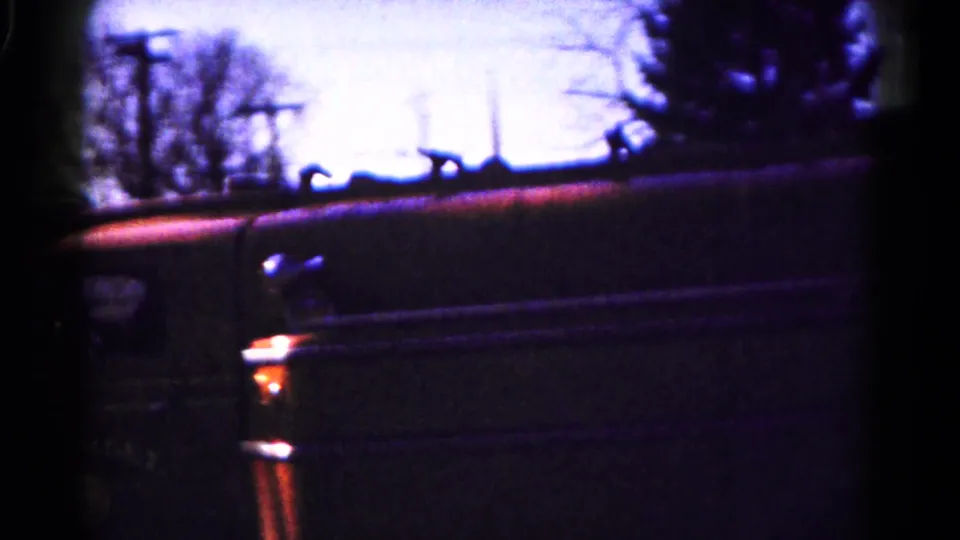 Close side view of the vintage fire engine, dark in exposure, with roadside trees and utility lines in the background.