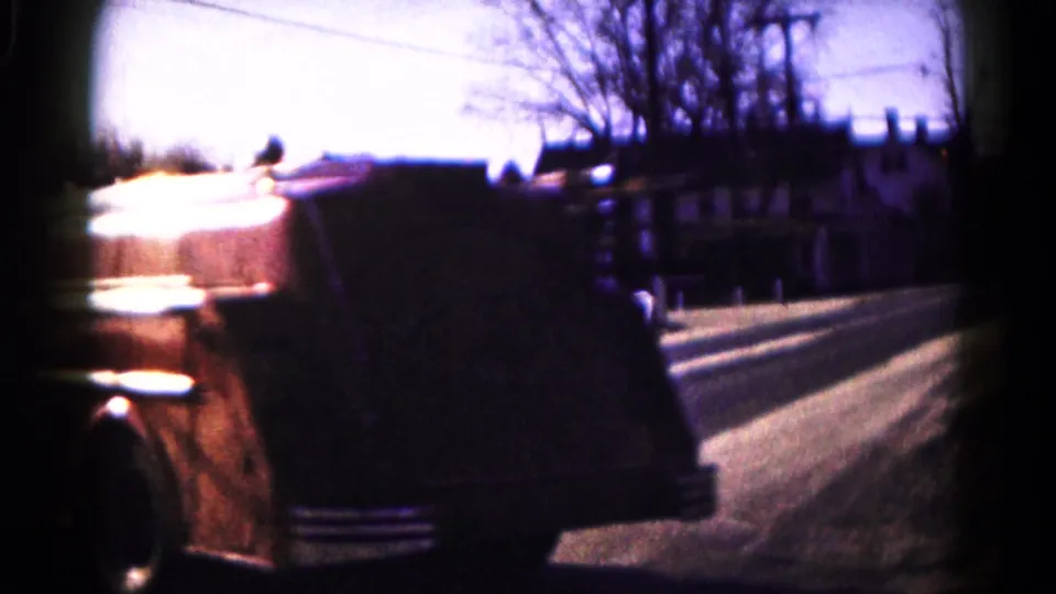 Rear view of the vintage fire engine continuing down a Hagerstown residential road, with a fence and bare trees alongside.