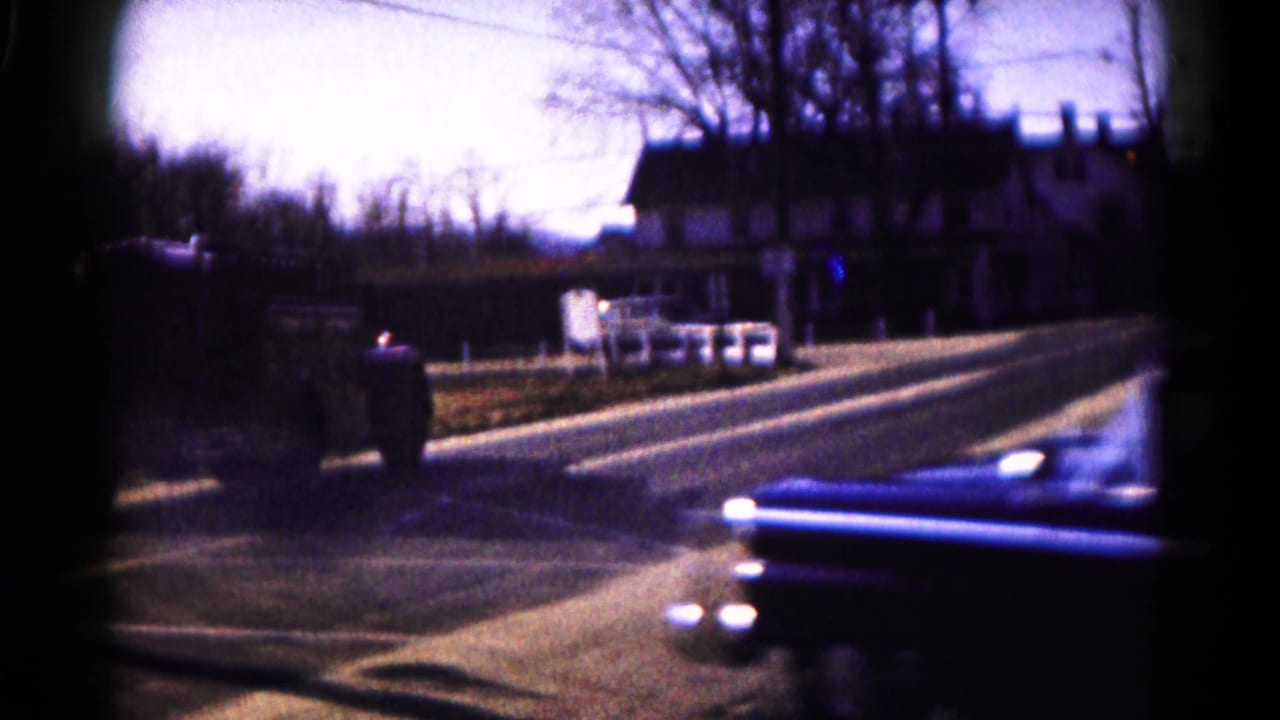 A blue early-1960s sedan turns across a Hagerstown street, with houses, bare trees, and roadside shadows in the background.