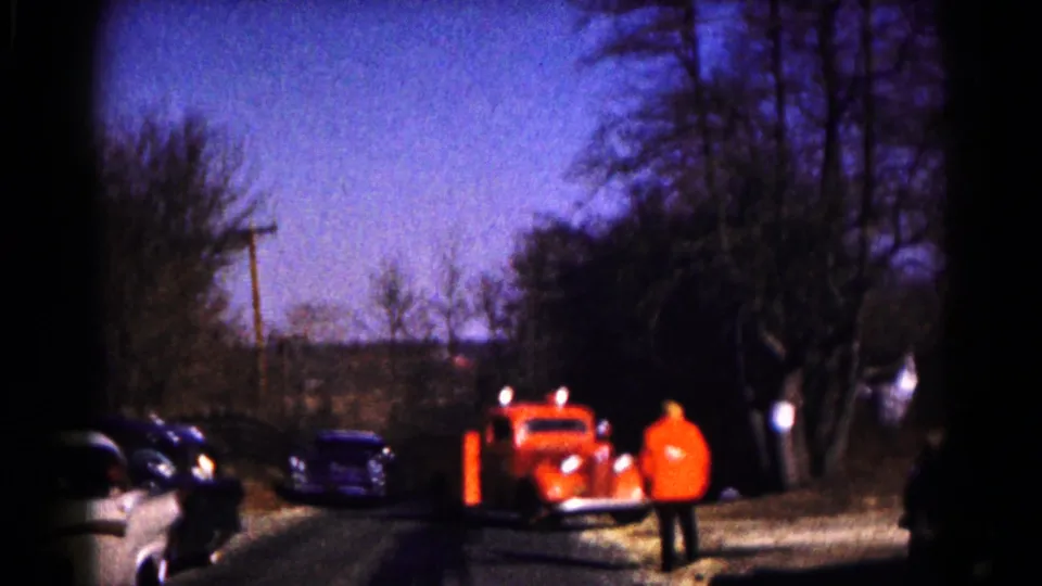 An orange tow truck is parked along a Hagerstown roadside as a person in a bright orange jacket stands nearby and cars line the street.