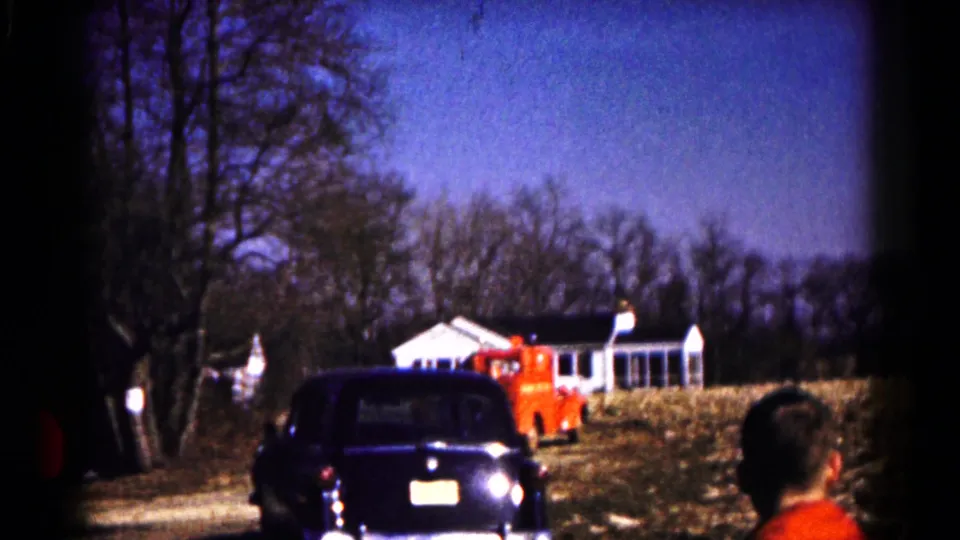 1961 Hagerstown frame showing the red fire truck farther up the driveway behind a dark car, with a bystander at the edge.