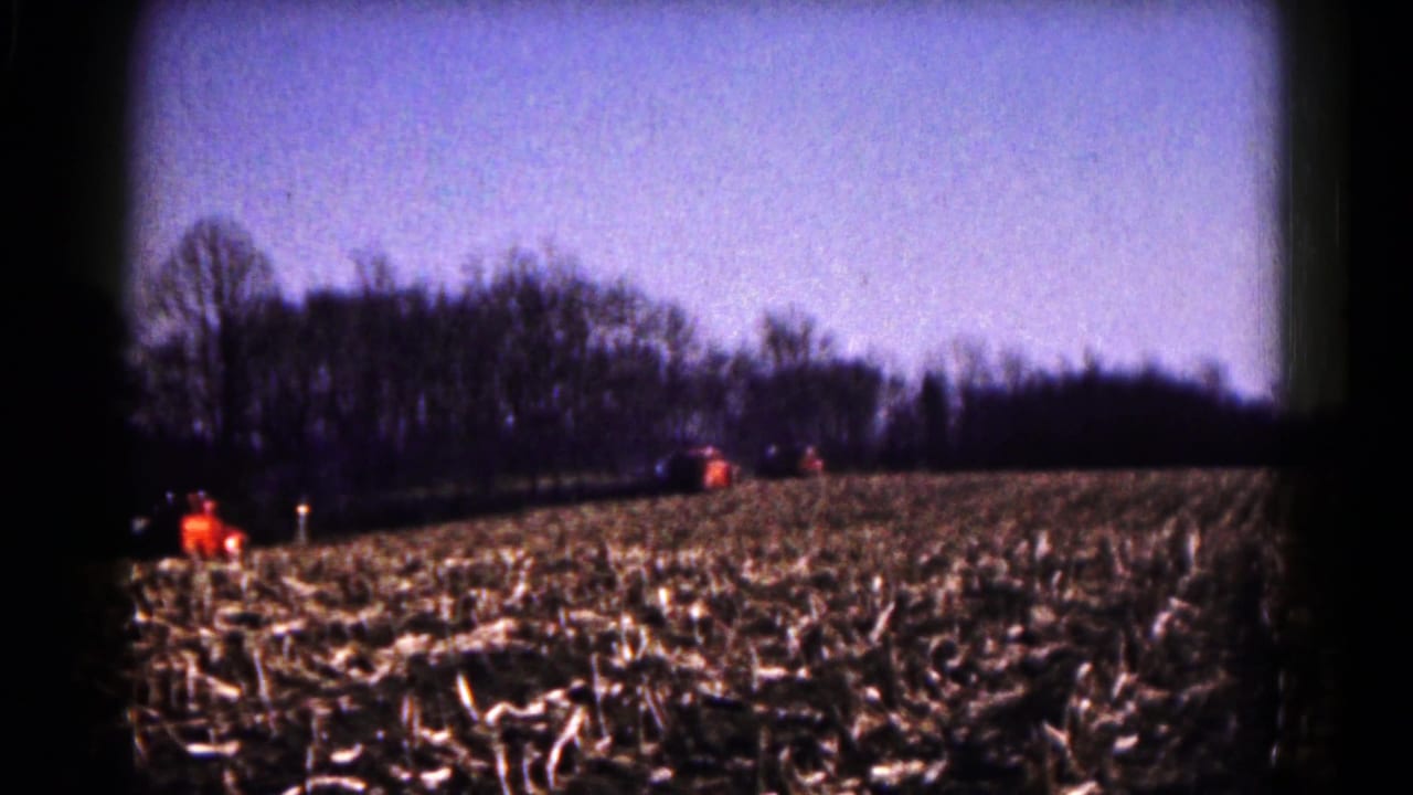1961 8mm home-movie view near Hagerstown, Maryland, showing a harvested field with distant orange tractors and leafless trees.