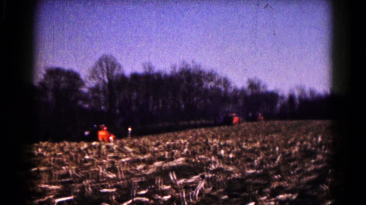 A rural Hagerstown-area field in 1961, with orange tractors moving across harvested corn rows beneath a clear sky.