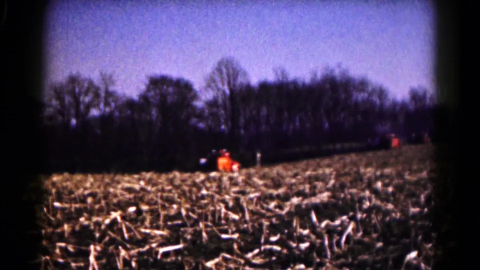1961 8mm frame from Hagerstown, Maryland, with small distant people near an orange tractor in a harvested autumn field.