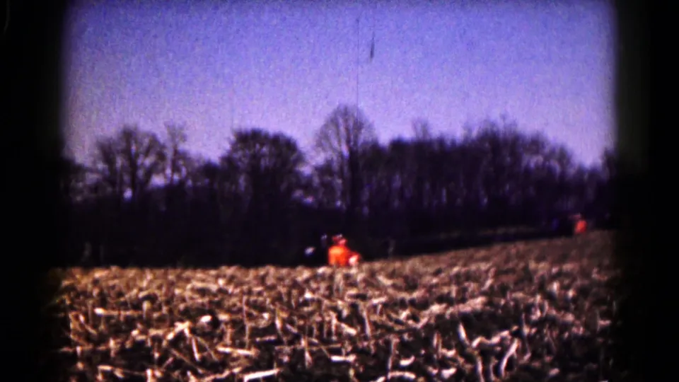 End frame of the 1961 farm scene, showing the tractor near the treeline beyond rows of cut field stubble.