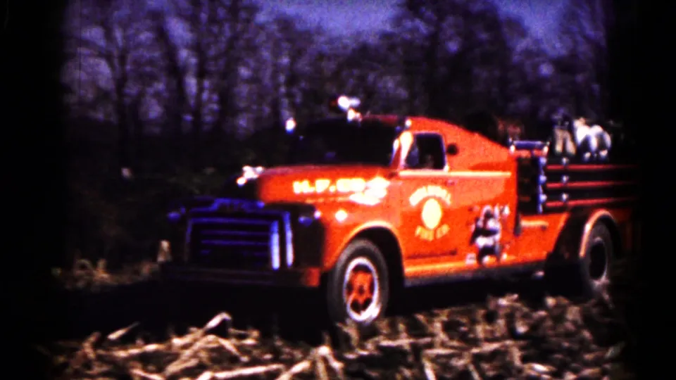 Closer 1961 home-movie view of a red Holmdel Fire Co. truck driving through a harvested field with equipment visible on the body.