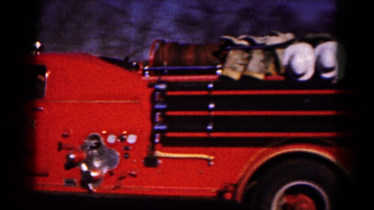 Close 1961 8mm view of a red Hagerstown fire truck side, showing hose reels, chrome fittings, and dark film edges.