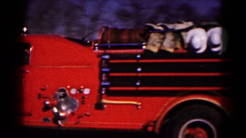 Close 1961 8mm view of a red Hagerstown fire truck side, showing hose reels, chrome fittings, and dark film edges.