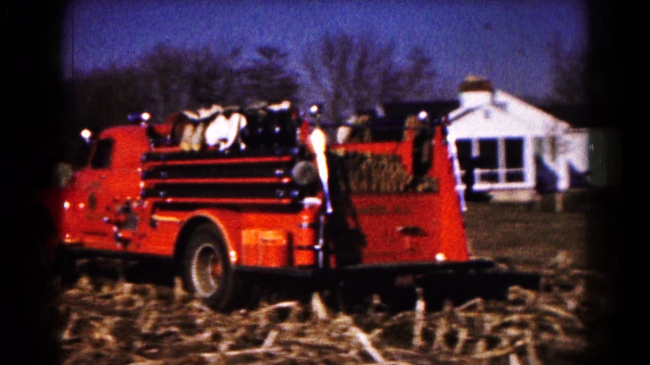 Red Hagerstown fire truck moves through a harvested field near a white farmhouse and bare trees in 1961 home-movie footage.