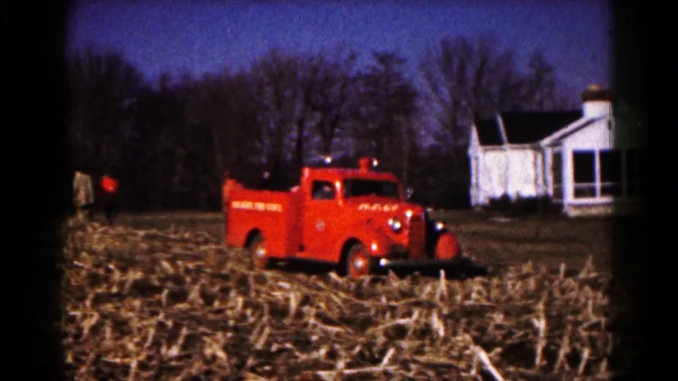 Red Hagerstown fire truck seen at a distance in a harvested cornfield, with a white house and tree line in the background.