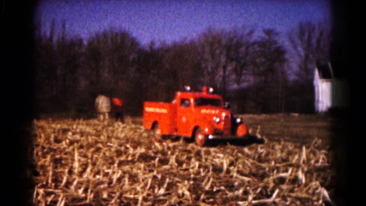 1961 Hagerstown 8mm frame showing a red fire truck in a harvested cornfield with trees and a small white structure behind it.