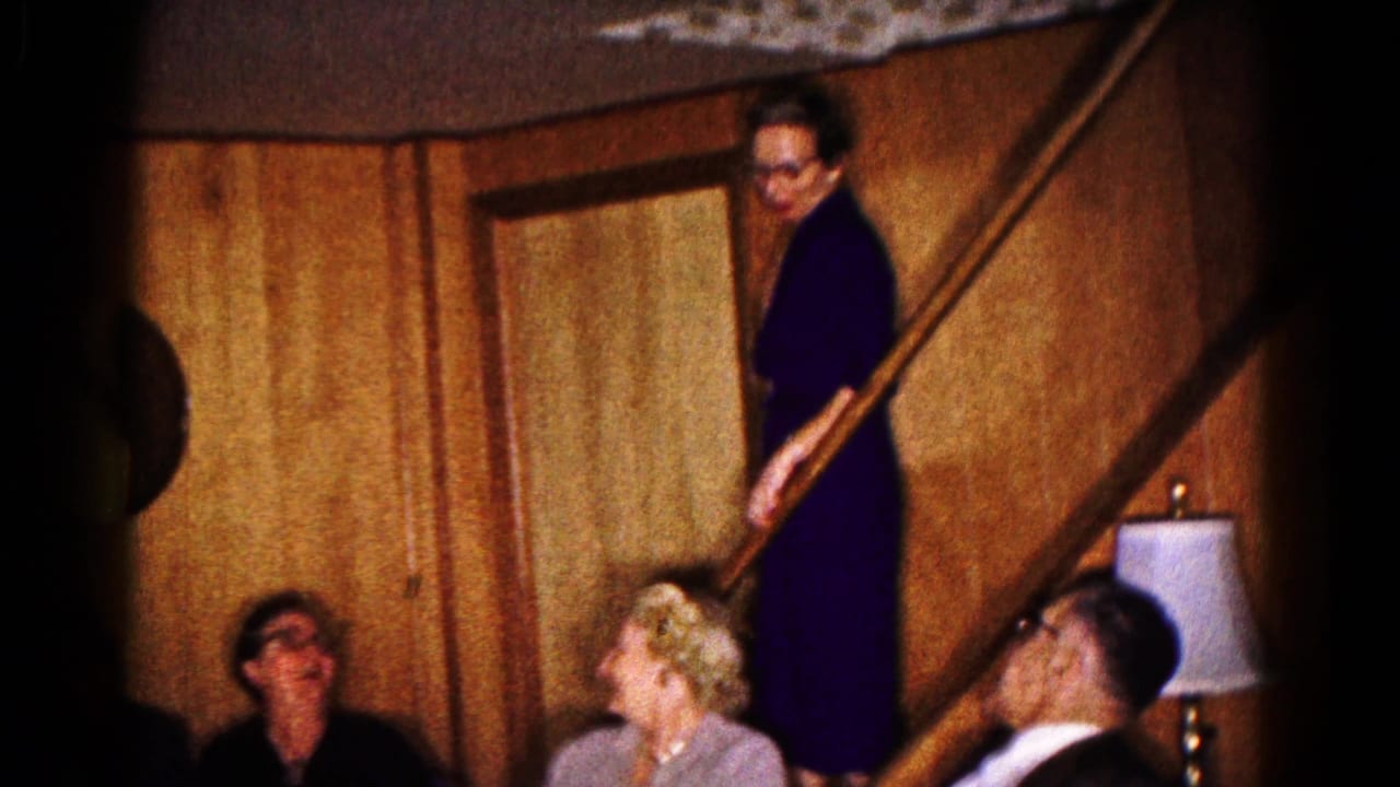 1961 Hagerstown frame with a woman on the stairs looking toward adults seated below beside a lamp in a private interior.