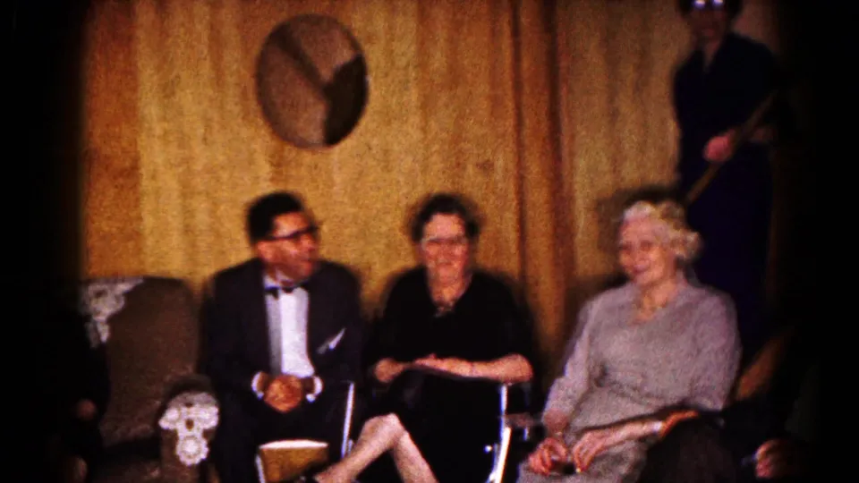 Formal-dressed older adults sit together in a wood-paneled Hagerstown basement, with round wall decor above them.