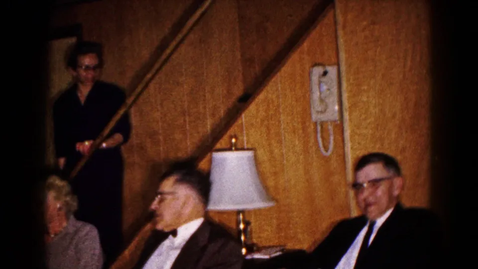 Adults in formal attire sit in a wood-paneled Hagerstown basement with a lamp, wall telephone, and staircase visible.