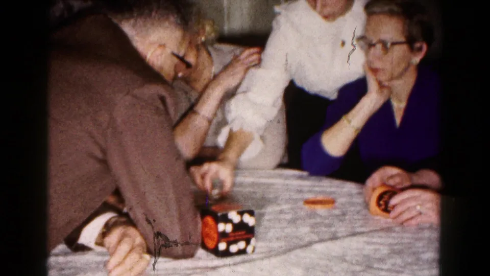 In a 1961 Hagerstown home interior, adults gather around a kitchen table during a tabletop game.