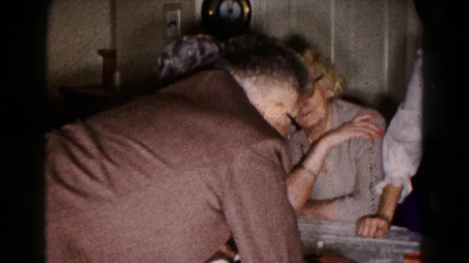In 1961 Hagerstown home-movie footage, older adults gather at an indoor table while a man leans toward a dice game.