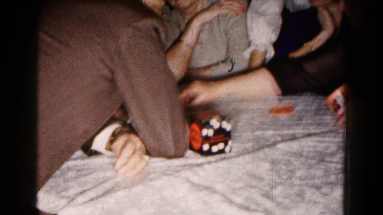Close view of a tabletop with adults' arms, a dark dice cup, and game pieces.