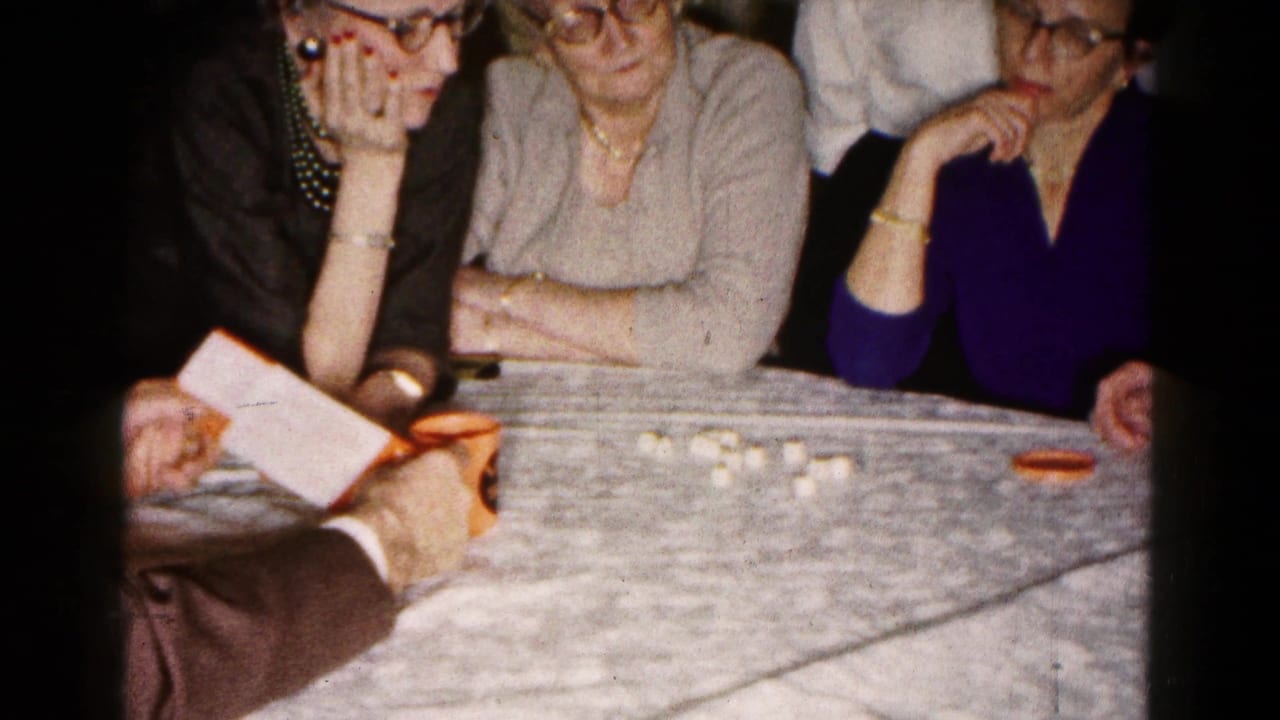 A man points at an open booklet while three women look toward the table.