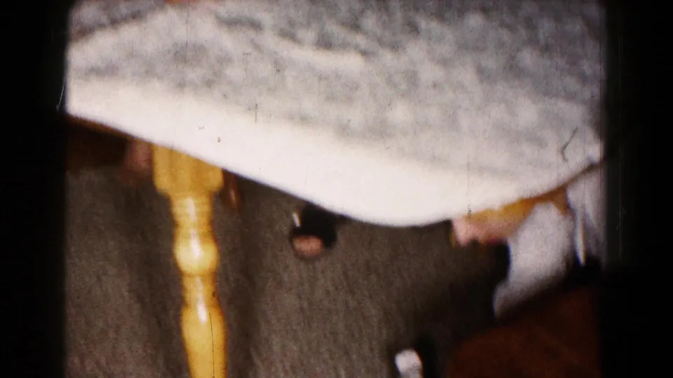 Indoor 1961 Hagerstown frame with table edge, wooden leg, adult clothing, and a person reaching toward the floor.
