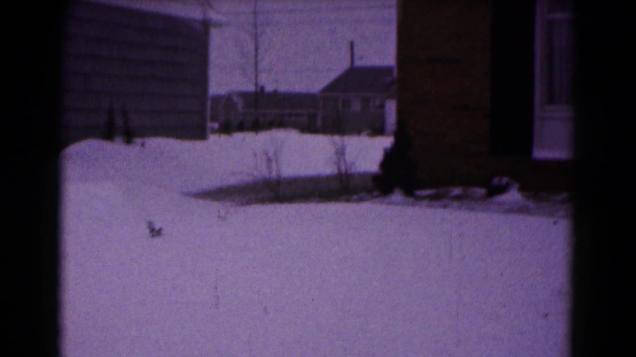 Snowy yard beside a brick house with white trim and a neighboring house in the background.