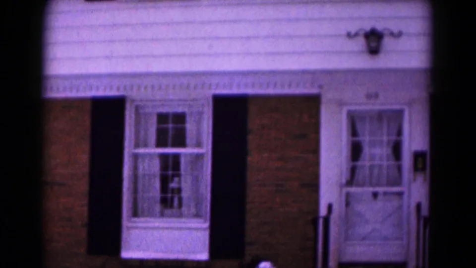 1961 Hagerstown home-movie frame showing the front door, windows, shutters, and snowy yard of a residence.