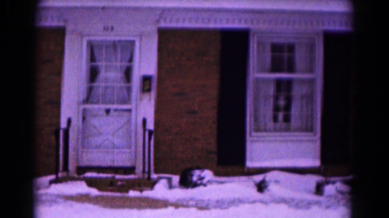 The camera holds on the snowy front entry of the Hagerstown brick home, with a white door, side window, shutters, and low shrubs.