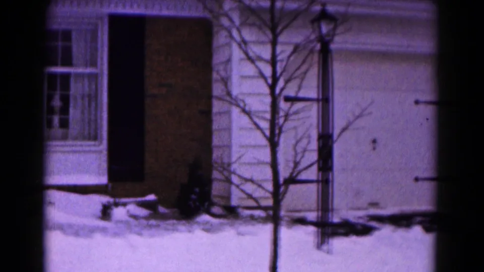 The pan reaches the side of the Hagerstown home, revealing a bare tree, lamppost, white garage door, brick wall, shutters, and snow-covered ground.