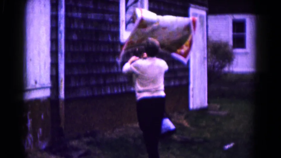 From behind, the woman adjusts the patterned quilt on the clothesline outside the shingled house in Hagerstown, Maryland.