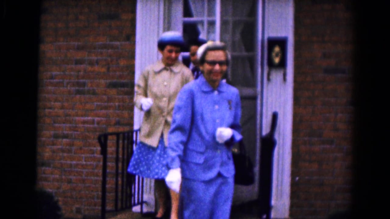 Two well-dressed women step from a brick building doorway.
