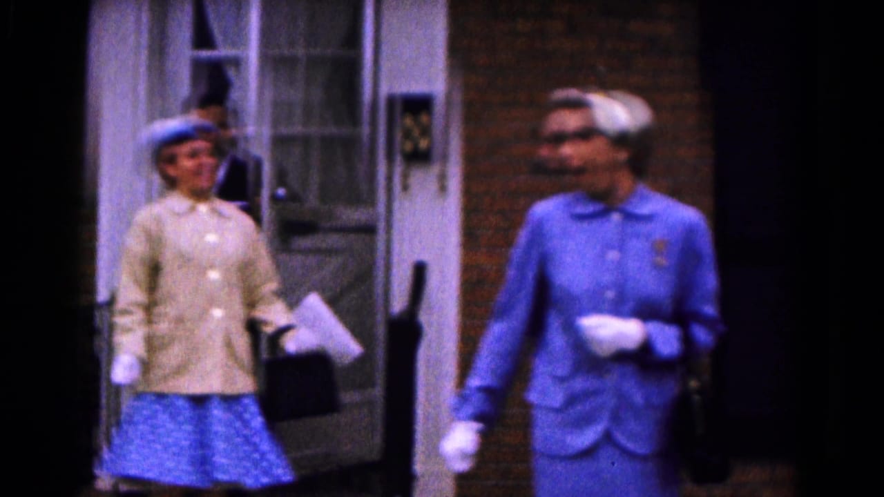 Two adult women in 1961 Hagerstown home-movie footage stand outside a brick building, one holding papers and a handbag.