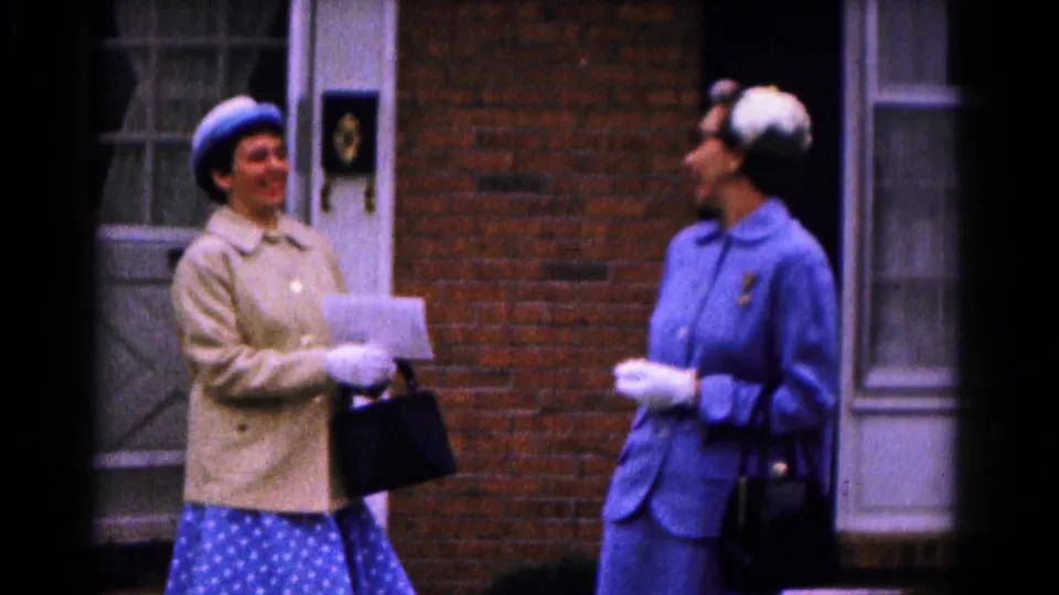 In the Hagerstown 1961 scene, two women in hats and gloves appear to smile and converse outside a brick building.