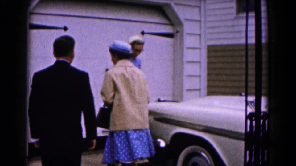 The boy and two women in Sunday clothing meet near a garage door and white car in Hagerstown, Maryland home-movie footage from 1961.
