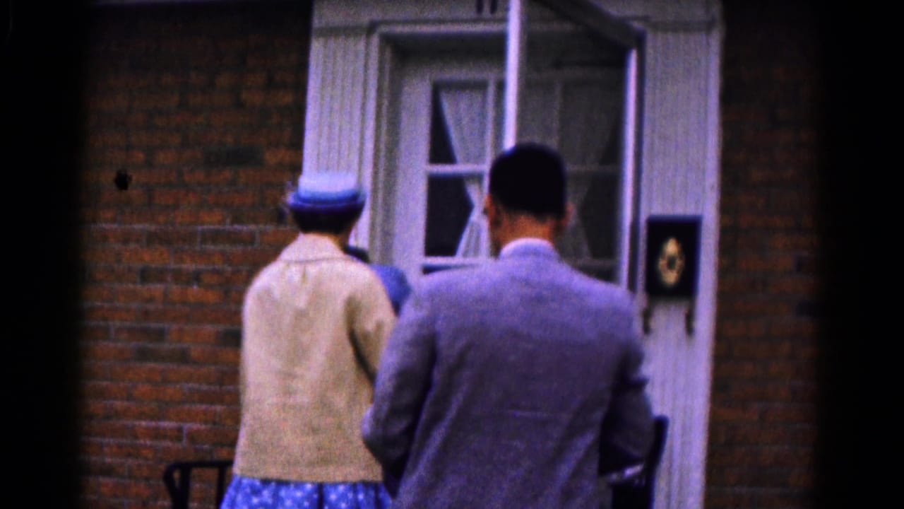 A man in a suit and a woman in a blue hat approach an open front door at a brick residence in Hagerstown, Maryland.