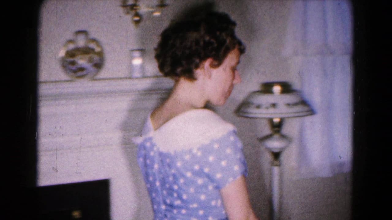 A young woman in a blue and white polka dot dress is seen from behind in a private Hagerstown living room, near a lamp and mantel.