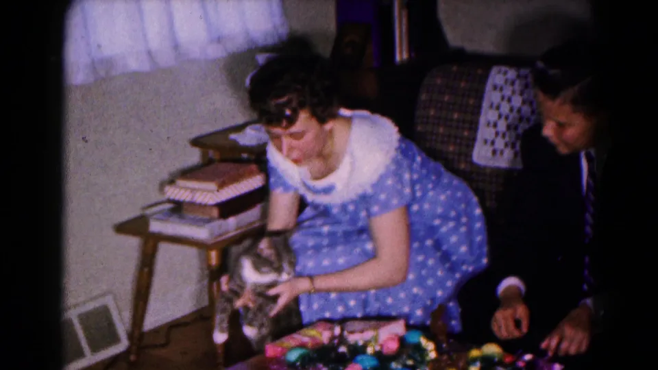 1961 Hagerstown frame showing a woman petting a grey and white cat with a suited man seated nearby in a home interior.