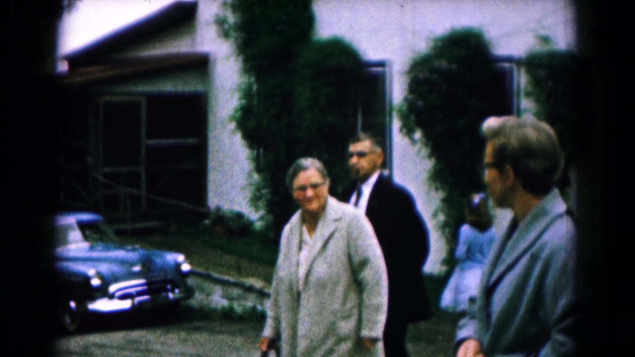 Adults walking outside a residence near a blue vintage sedan.