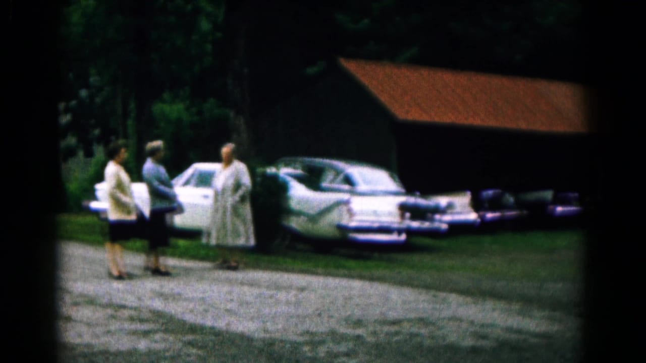 In 1961 Hagerstown, Maryland, three women talk beside mid-century parked cars near trees and a red-roofed barnlike structure.